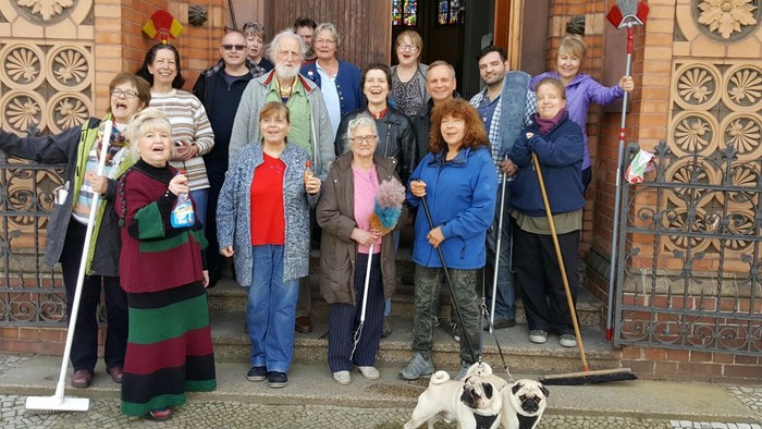 Gruppe von Menschen, die Besen und Kehrbleche halten und vor einem geschmückten Gebäude posieren, mit einem Hund in der Nähe.