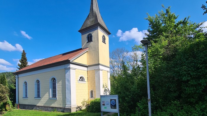 Idyllische Kirche mit hohem Kirchturm in einer üppigen, grünen Landschaft an einem sonnigen Tag.