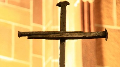 Kreuz aus zwei alten Nägeln vor einer hellen Ziegelwand