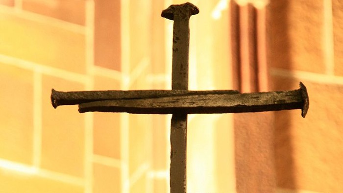 Kreuz aus zwei alten Nägeln vor einer hellen Ziegelwand