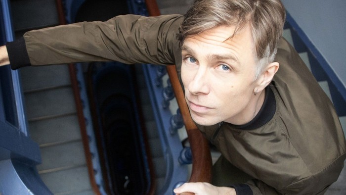 En person læner sig over gelænderet på en spiraltrappe med et eftertænksomt udtryk.