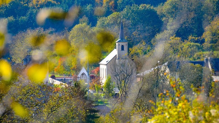 En lille kirke i en skovklædt landsby med faldende bakke.