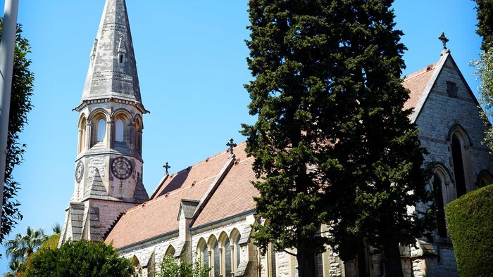 En kirke med spir med tårn og klokke, omgivet af træer og buske