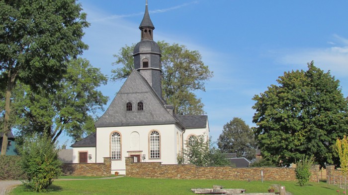 Kleine weiße Kirche mit schwarzem Dach und Turm auf grünem Rasen