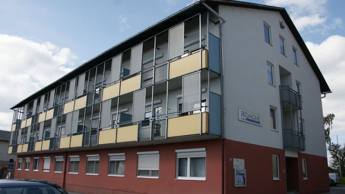 Moderne mehrstöckige Wohnanlage mit Balkonen, rotem Sockel und Beschilderung an der Seite.