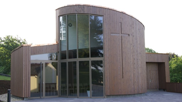 Moderne Holzkirche mit großem Glasfenster und Kreuz an der Fassade