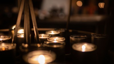 Mehrere brennende Kerzen in Glashaltern sind auf einer dunklen Oberfläche arrangiert und schaffen eine warme und friedvolle Atmosphäre.