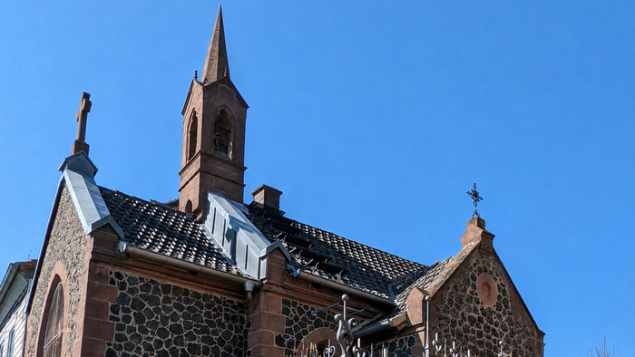 Historische Kirche mit markantem roten Backstein und Schieferdach unter klarem blauem Himmel.
