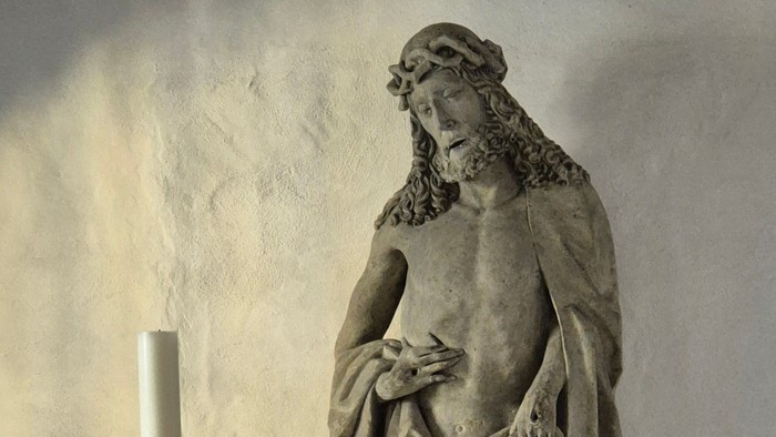 Steinfigur des leidenden Christus auf Steinsockel mit Osterkerze auf einem goldenen Leuchter