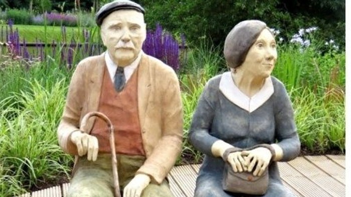 Ein älteres Paar sitzt auf einer Bank in einem Garten.