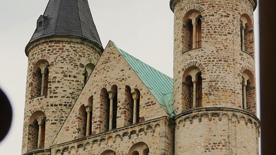 Historische Steinkirche mit Zwillingstürmen und grün gedeckten Spitzen vor bewölktem Himmel.