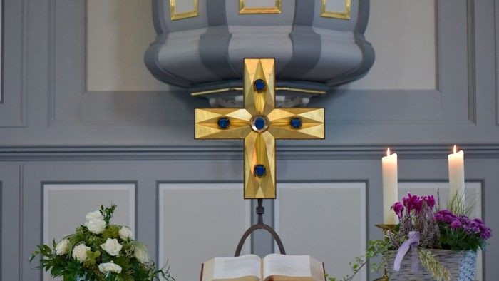 Eleganter Altar mit einem verzierten goldenen Kreuz, einem aufgeschlagenen Buch und Blumengestecken mit brennenden Kerzen.