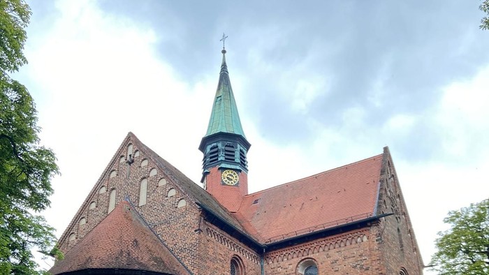 Historische Backsteinkirche mit spitzem Turm und Bogenfenstern inmitten eines grünen Rasens.