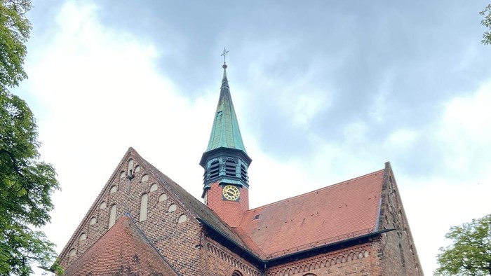 Historische Backsteinkirche mit spitzem Turm und Bogenfenstern inmitten eines grünen Rasens.