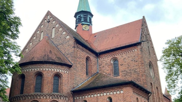 Historische Backsteinkirche mit spitzem Turm und Bogenfenstern inmitten eines grünen Rasens.
