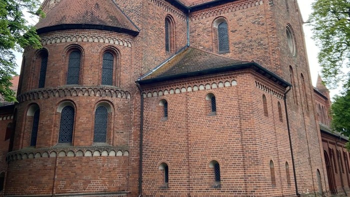 Historische Backsteinkirche mit spitzem Turm und Bogenfenstern inmitten eines grünen Rasens.