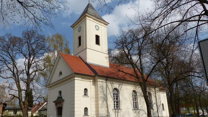 Kleine weiße Kirche mit rotem Dach und Turm in parkähnlicher Umgebung