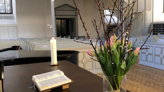 Eleganter Kircheninnenraum mit einem Holztisch, auf dem ein offenes Buch und eine Vase mit frischen Blumen stehen.