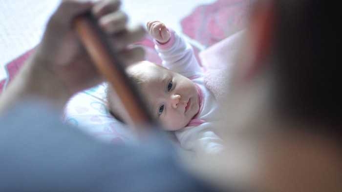Et spæd barn holder en træstang og ser opad.