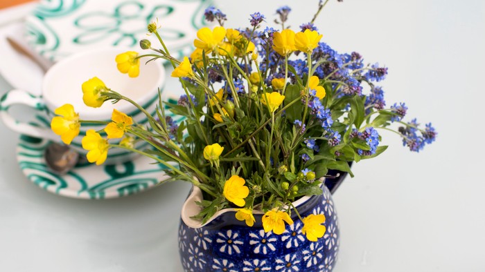Blumen in blauem Gefäß auf weißem Tisch