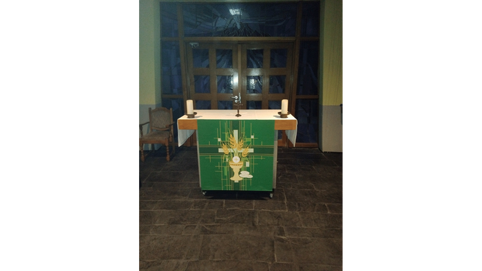 Ein ruhiger Altar mit grünem Tisch, Kerze und religiösen Symbolen in einer schwach beleuchteten Kapelle.