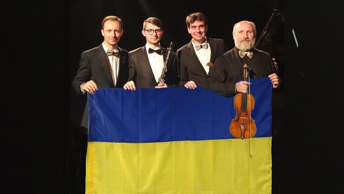 Vier Musiker halten eine ukrainische Fahne. Einer hält zudem eine Klarinette und ein anderer eine Geige.