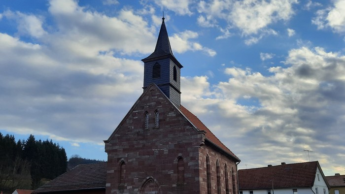 Kirche mit hohem Kirchturm vor teilweise bewölktem Himmel.
