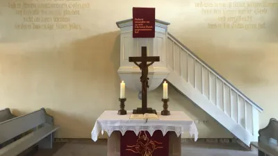 Ein ruhiger Kirchenaltar mit einem Kreuz, Kerzen und religiösen Inschriften an den umliegenden Wänden.