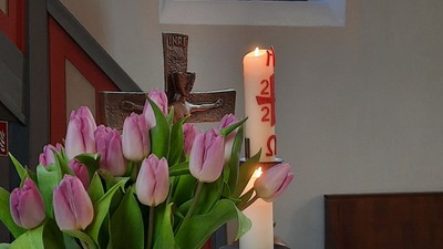 Vase mit Tulpen, Kerze und Buch auf dem Tisch unter einem Buntglasfenster.