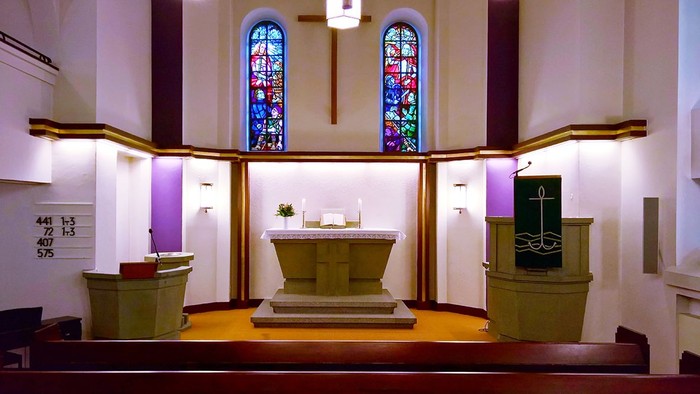 Elegante Kircheninnenausstattung mit Buntglasfenstern, Altar und Taufbecken mit religiösen Symbolen.
