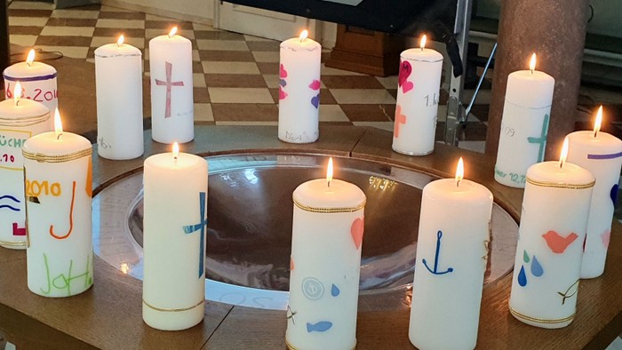 Verzierte Kerzen im Kreis angeordnet mit brennenden Flammen, jede mit persönlichen Botschaften oder Symbolen beschriftet.