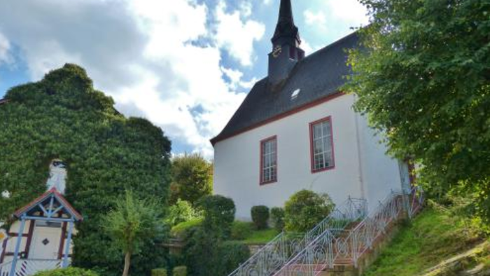 Idyllische weiße Kirche mit steilen Treppen und üppigem Grün an einem sonnigen Hang.