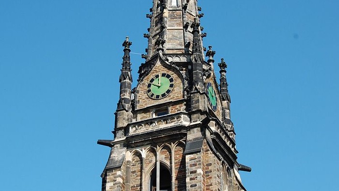 Der Kirchturm hat ein grünes Zifferblatt und spitze Bögen.
