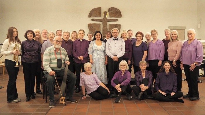 Gruppe af mennesker, der poser foran et kors; nogle står, nogle sidder, iført afslappet og religiøst tøj.