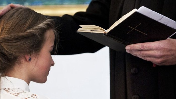 En ung pige ser på en bog, som en mand i mørkt kostume holder op for hende