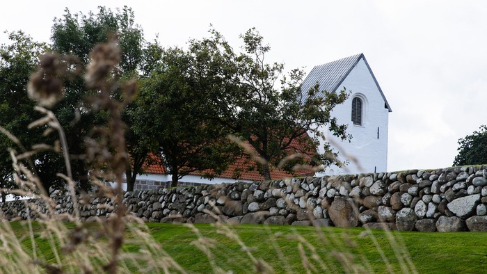 En lille hvid kirke bag en stenmur og græs.