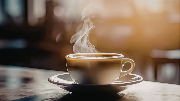 Heißer dampfender Kaffee in einer weißen Tasse auf einer Untertasse, der aromatischen Dampf verströmt.