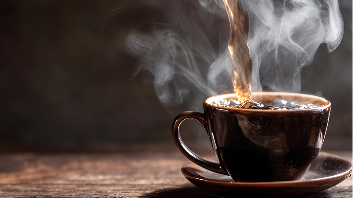 Heißer dampfender Kaffee in einer dunklen Tasse auf einer hölzernen Untertasse mit aufsteigendem Dampf.