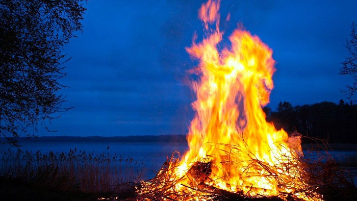 En stor bål brænder ved kanten af et vandområde om natten