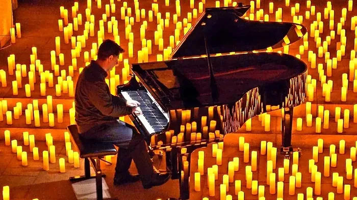 Eine Person spielt Klavier, umgeben von zahlreichen brennenden Kerzen in einer feierlichen, warm beleuchteten Atmosphäre.