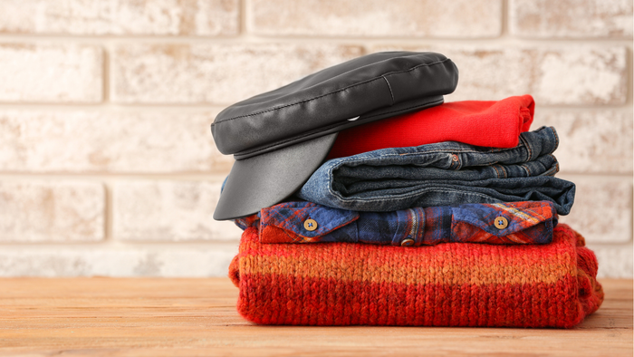 Ein ordentlich gestapelter Stapel Kleidung und eine schwarze Tasche auf einer Holzoberfläche vor einer Backsteinmauer.