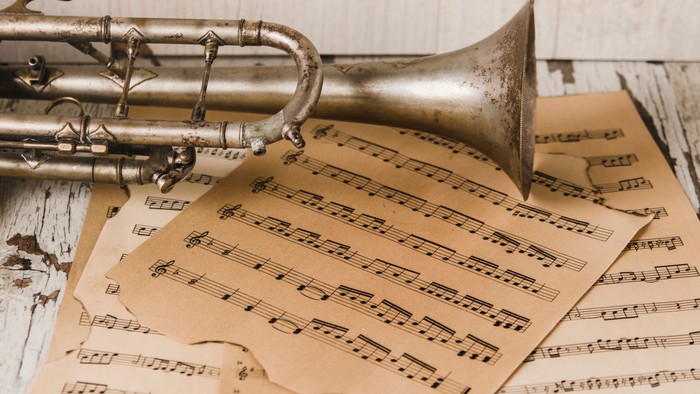 Eine alte Trompete liegt neben vergilbten Notenblättern auf einer rustikalen Holzoberfläche.
