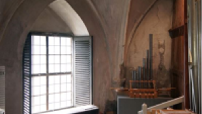 Ein ruhiger Raum mit gewölbten Steinwänden, einer Bank und einer Orgel an einer Wand nahe einem Fenster.