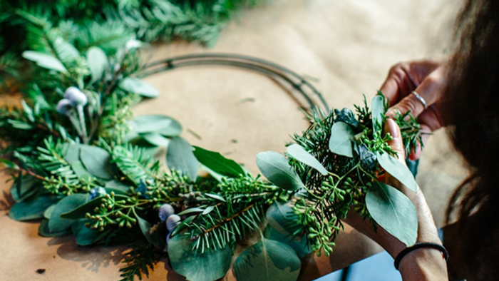 A person is crafting a wreath from greenery and eucalyptus leaves.