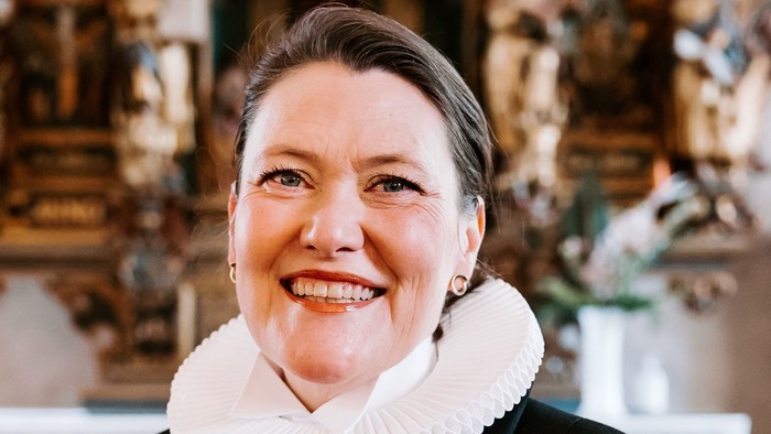 En kvinde i sort jakke med hvid krage står foran en prægtig altertavle.