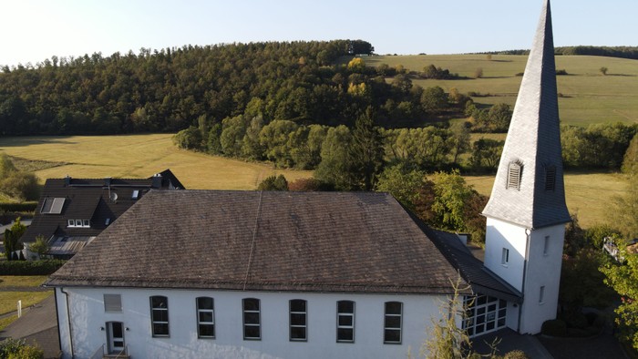 Weißes Gebäude mit spitzem Turm in ländlicher Umgebung