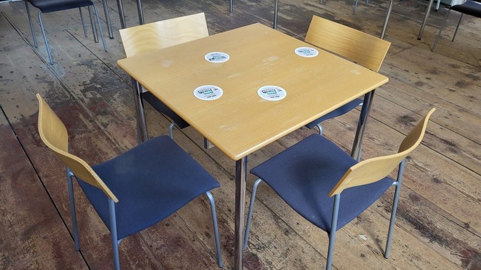 Leerer Holztisch mit blauen Polsterstühlen und Metallgestellen in einem geräumigen Raum.