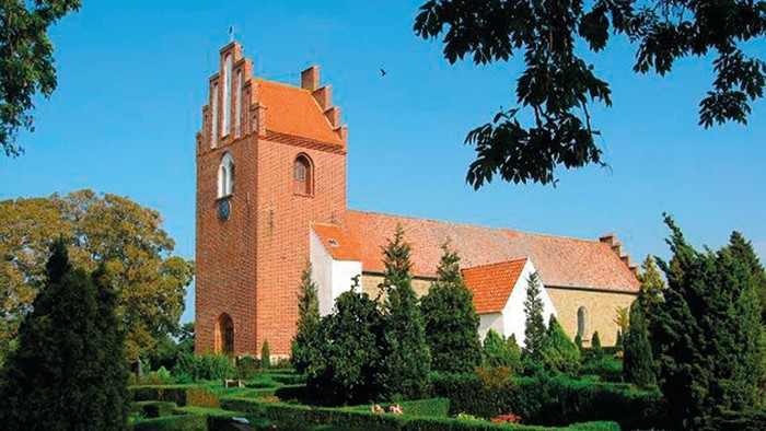 En rød murstenskirke med tårn og omgivelser med træer og buske