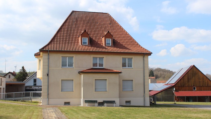 Ein charmantes zweistöckiges Haus mit rotem Ziegeldach in einer grünen, ländlichen Landschaft.