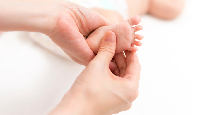 Hände, die sanft die Füße eines Neugeborenen massieren oder untersuchen.